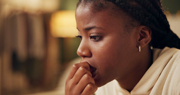 A young black woman at home with a concerned, anxious expression on her face, biting her nail