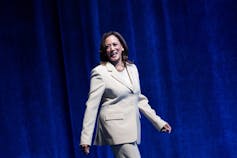 A Black woman who is smiling proudly walks on a stage before giving a speech.
