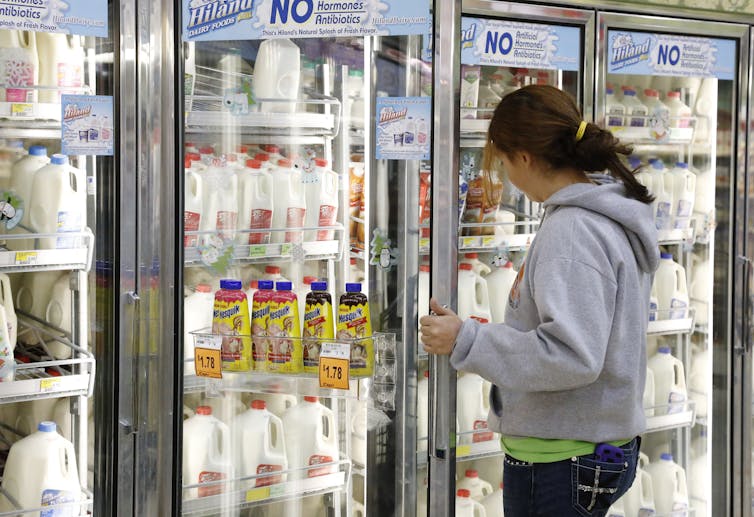 A young woman in a store opens the door to refrigerator case filled with milk products.