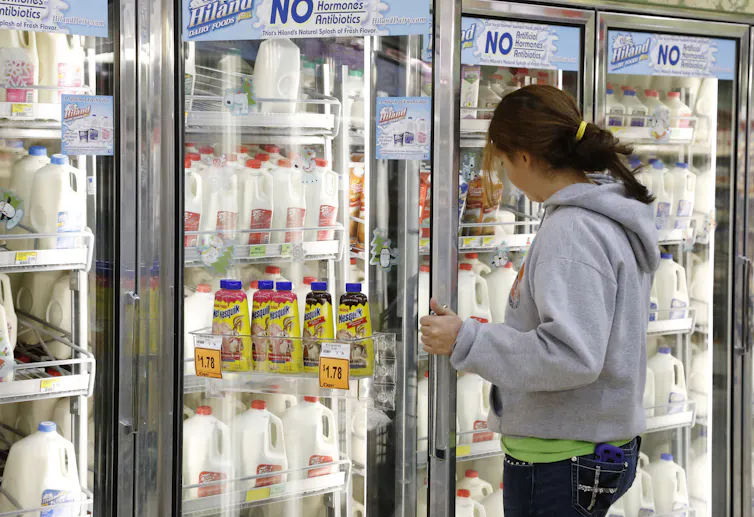 A young woman in a store opens the door to refrigerator case filled with milk products.