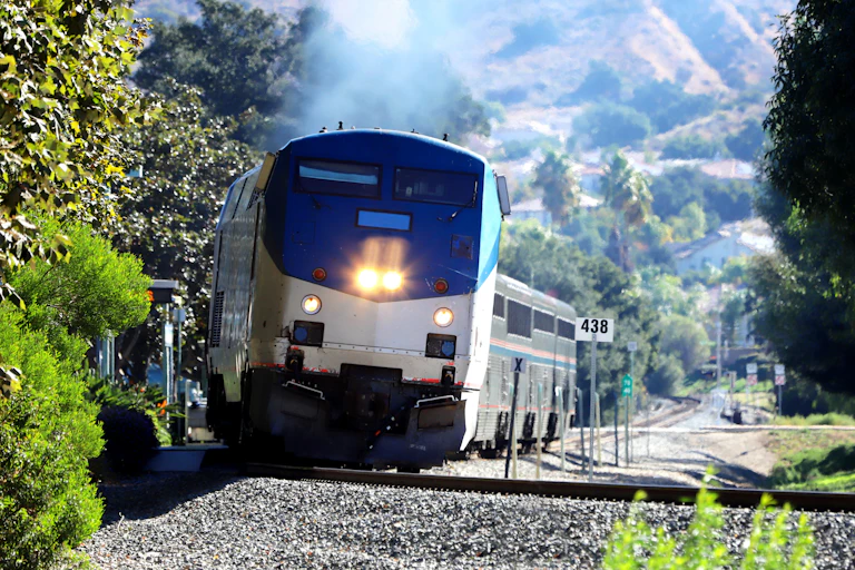 A train heads up a track as mountains and trees stand in the background.