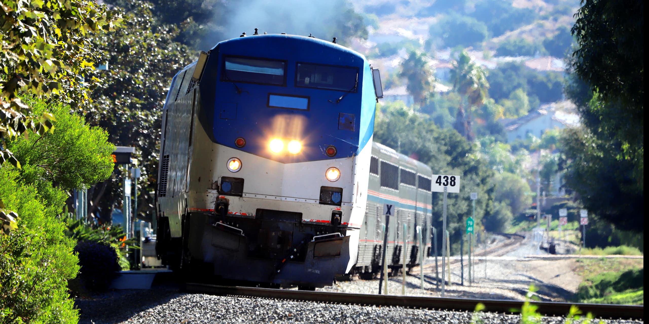 A train heads up a track as mountains and trees stand in the background.