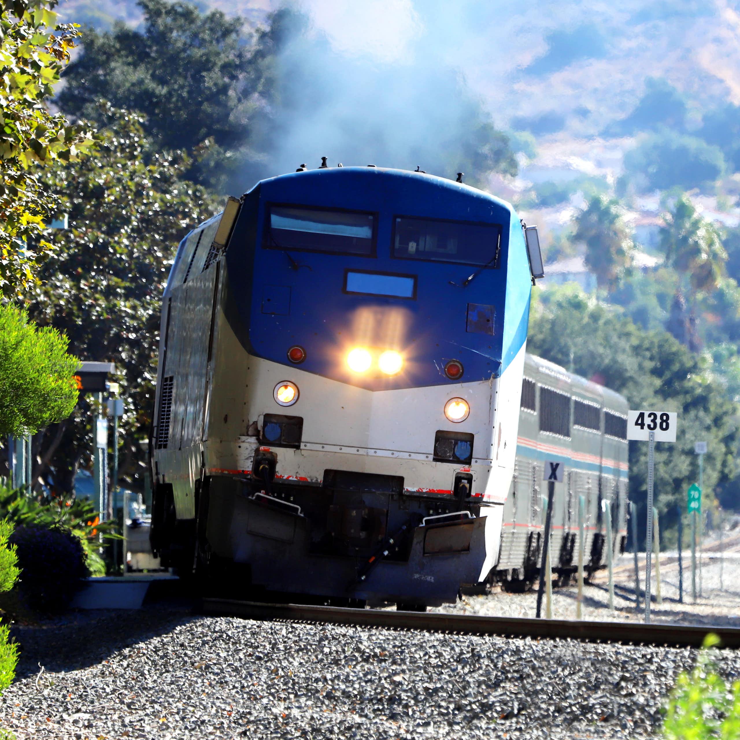 A train heads up a track as mountains and trees stand in the background.