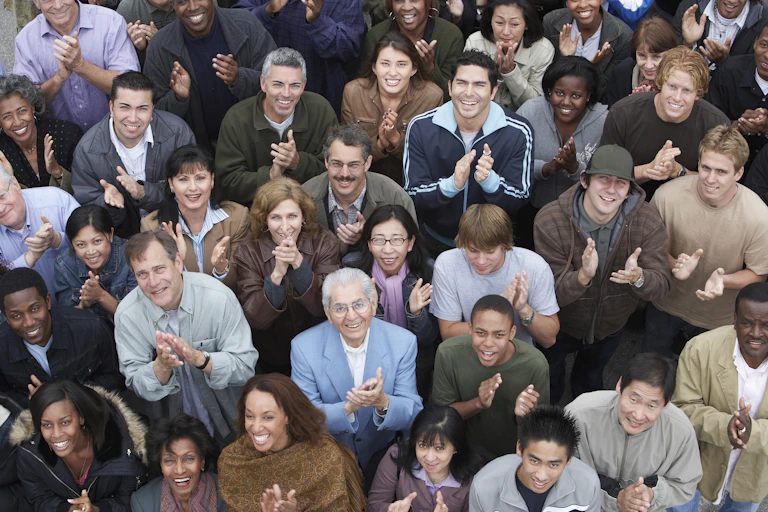 A crowd of people smiling and clapping as they look up, seen from above.