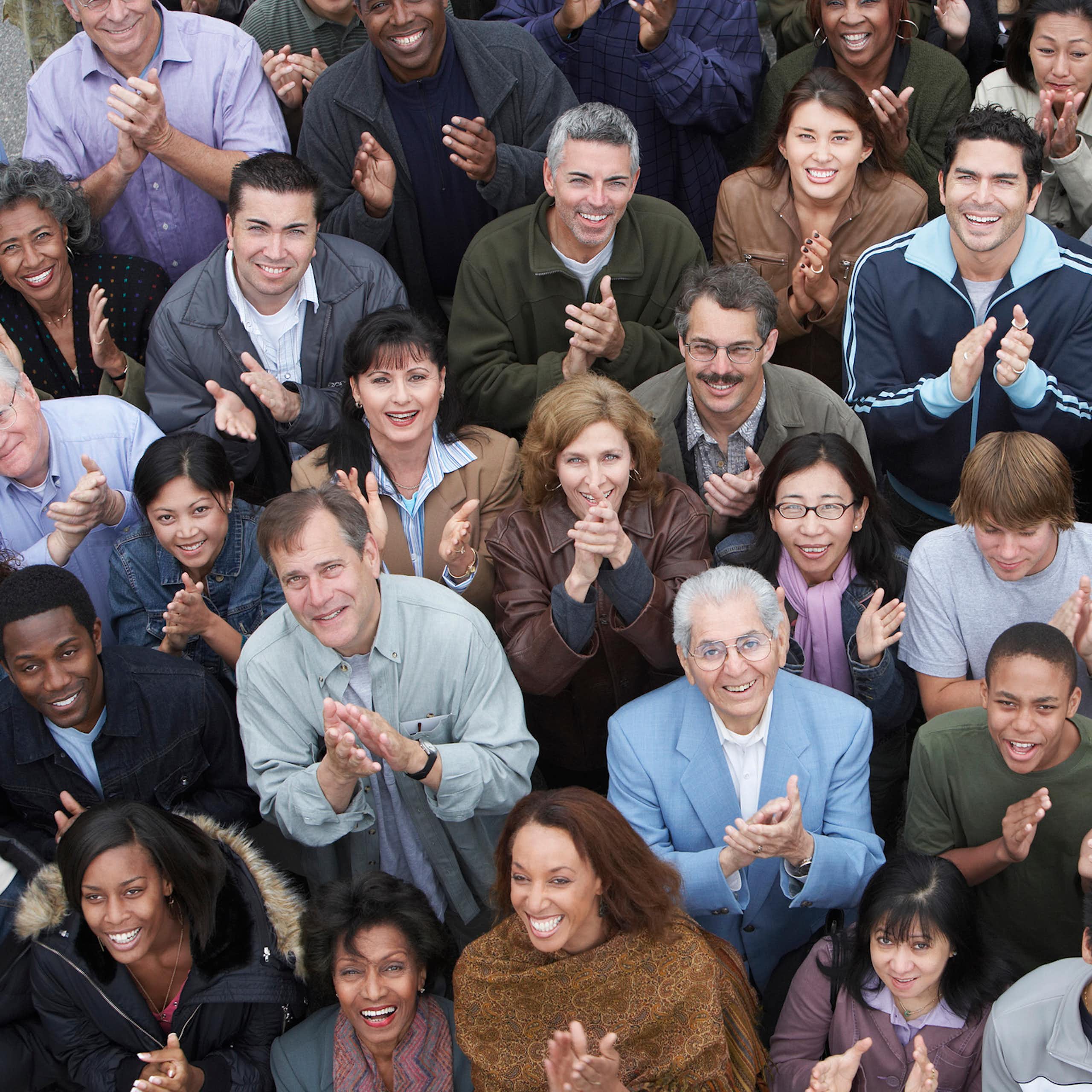 A crowd of people smiling and clapping as they look up, seen from above.