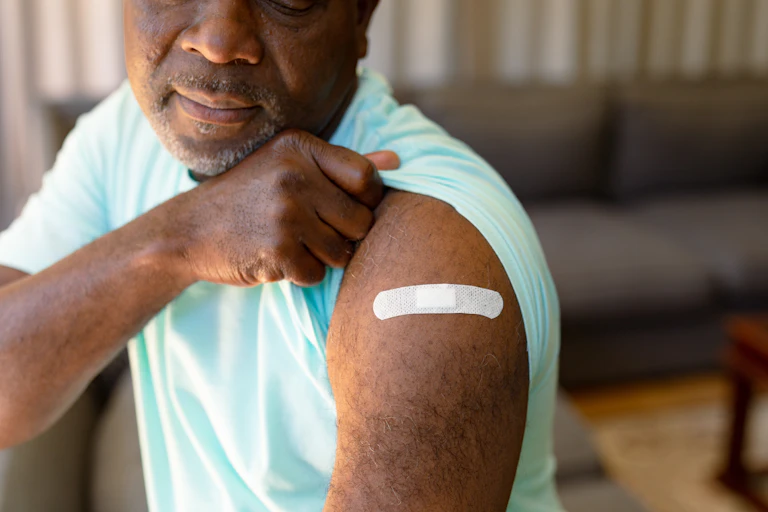 A man pulling up his sleeve to reveal a bandaid on his upper arm.