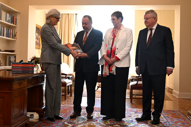 A woman accepts a thick document from three people