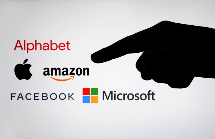 Silhouette of a finger pointing at the logos of big tech companies.