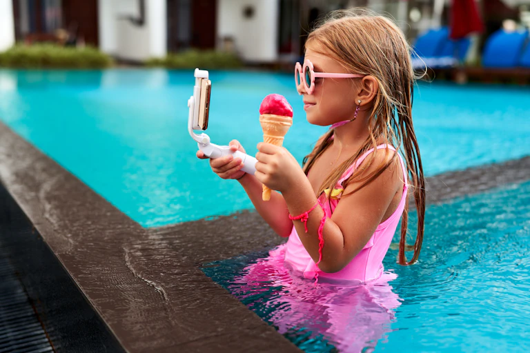 A little girl in a pink tutu stands in a pool taking a selfie.