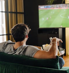 Man holding drink watching a soccer match on TV