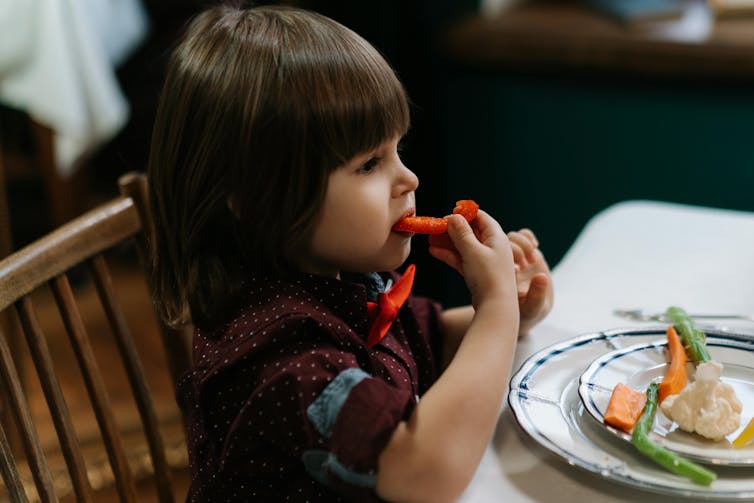 A small child eats vegetables.