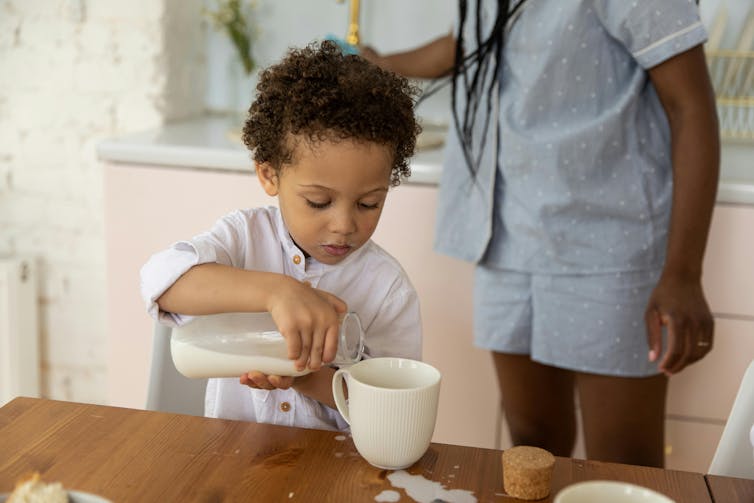 Toddler pours milk into a cup