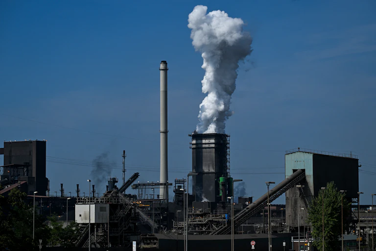 Installation industrielle de hauts fourneaux. De la fumée s'échappe d'une cheminée.