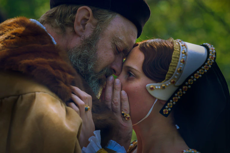 Jude Law as Henry VIII holds his hand over the mouth of Alicia Vikander as Katherine Parr.
