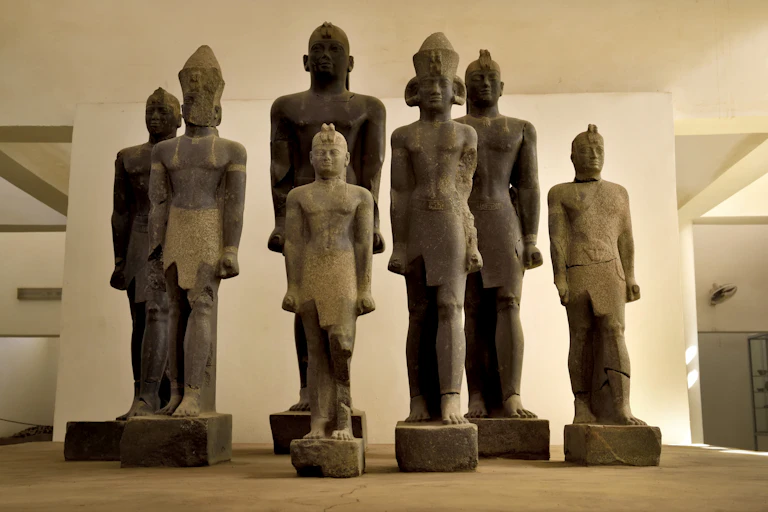 Giant stone sculptures of men tanging in size and angular an stylised, stand in a group of seven.