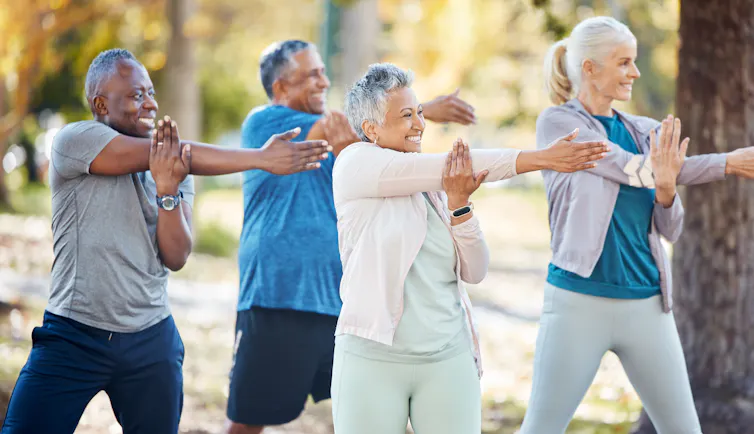 Four older adults in fitness clothes stretching outdoors