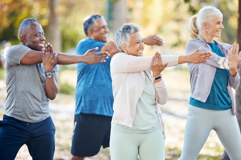 Four older adults in fitness clothes stretching outdoors