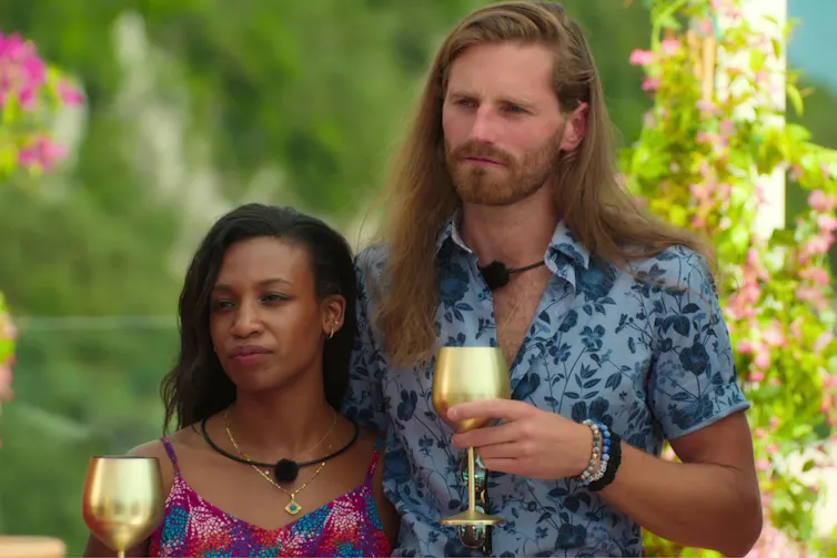a serious looking woman and a tall man hold gold wine glasses.