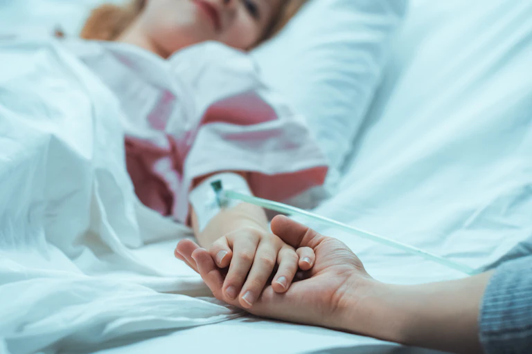 An adult holding the hand of a child in a hospital bed.
