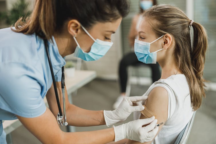 A nurse applies a bandaid to a girl's upper arm.