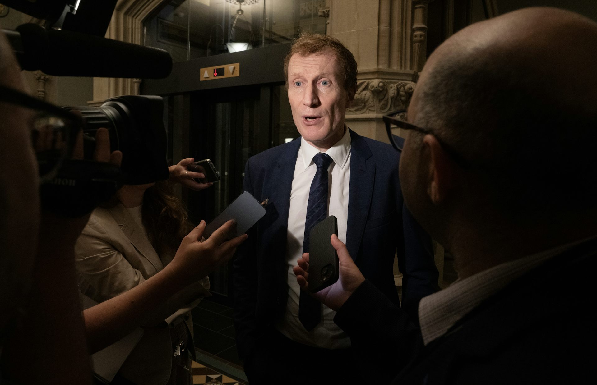 A man in a suit in the middle of a media scrum.
