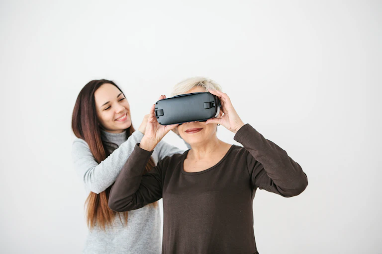 Une senior porte un casque de réalité virtuelle. Une jeune femme l'aide à la positionner.