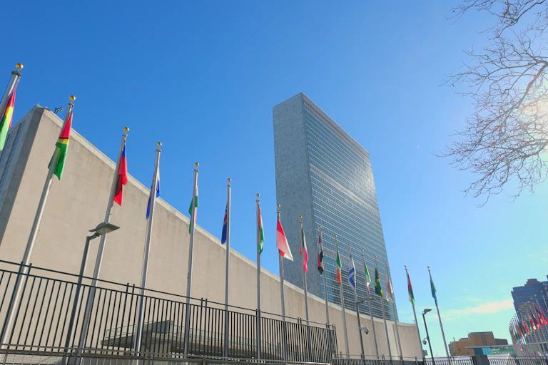 A curved building with a row of flags in front of of it in a winter's day. A taller rectangular tower is behind it.