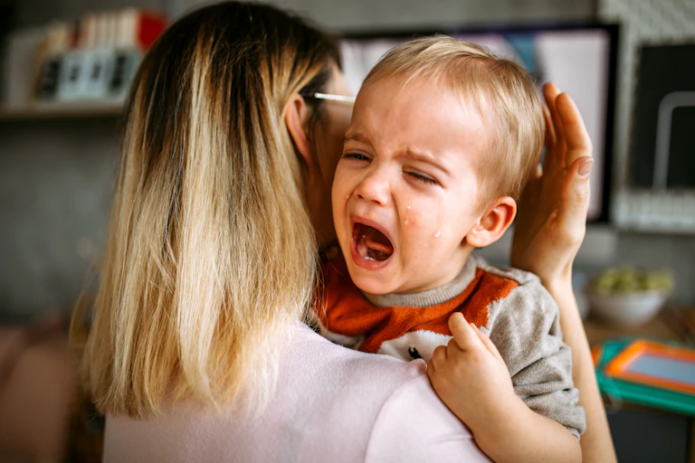 woman holds crying toddler up to her shoulder
