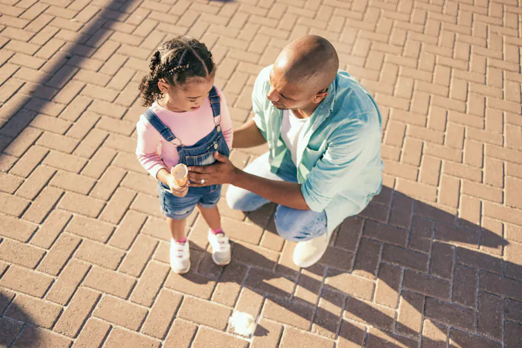 man kneels comforting girl holding a cone with her ice cream on the ground