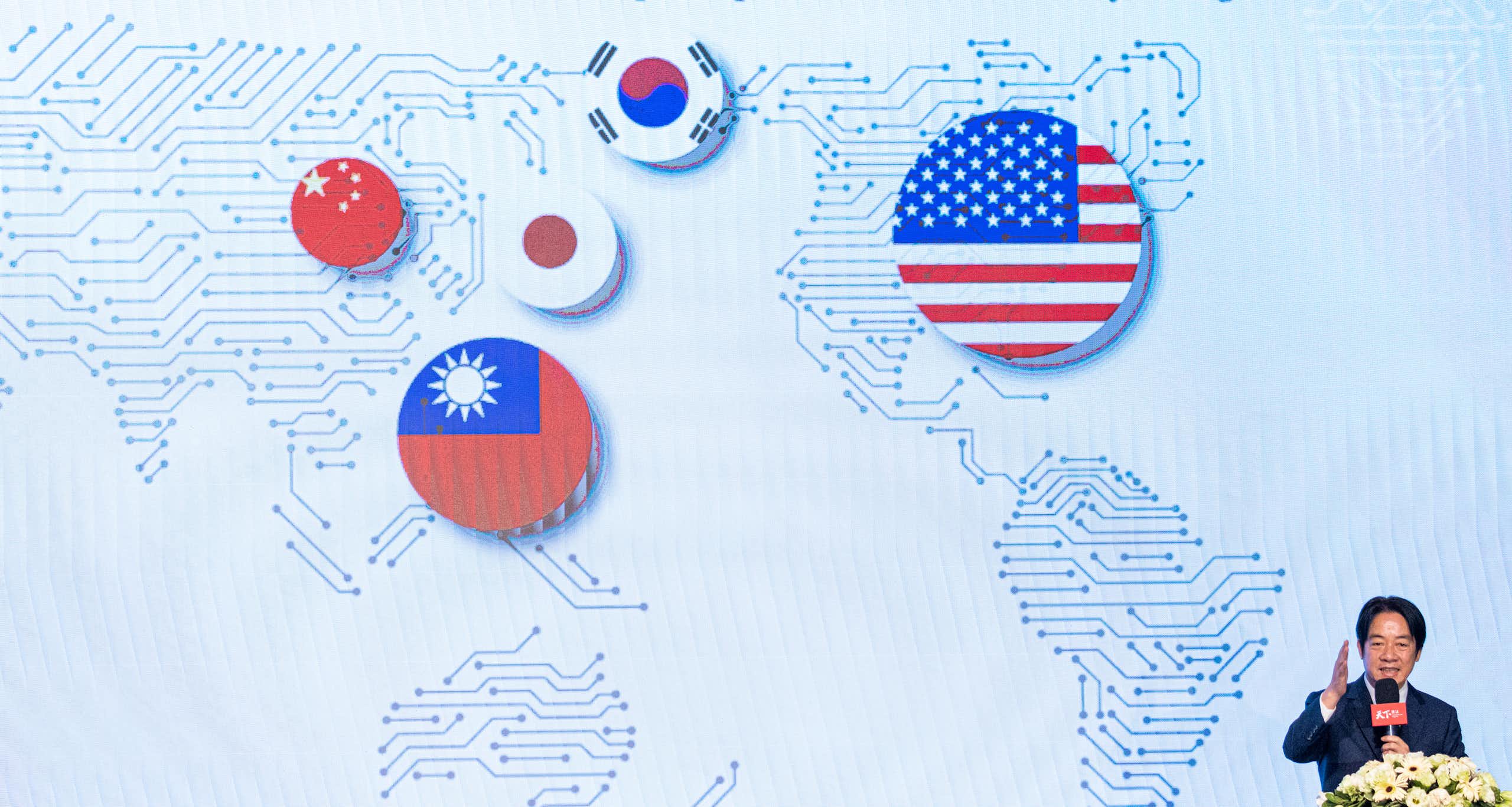 A man speaks at a microphone in front of a map with flags on it.