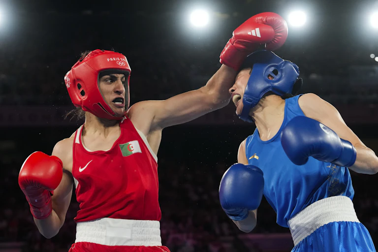 A woman in red boxing gear fights another woman in blue boxing gear.