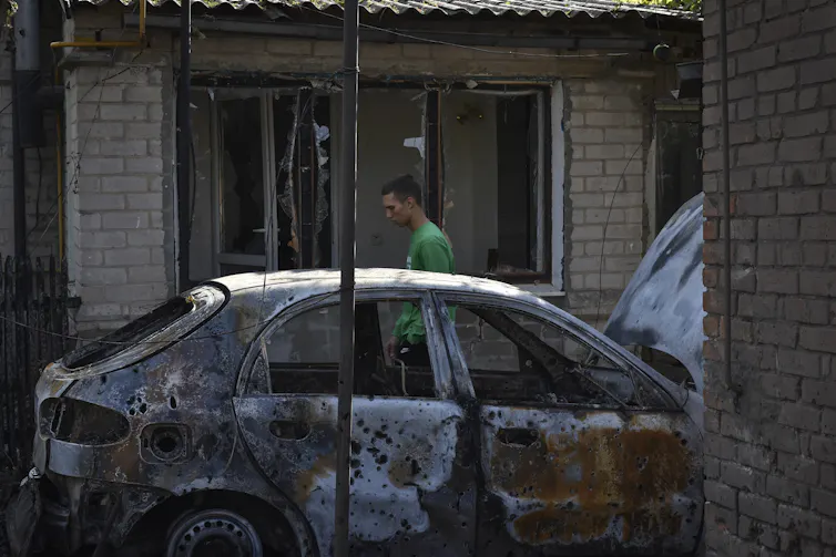 A man walks past a burned-out car