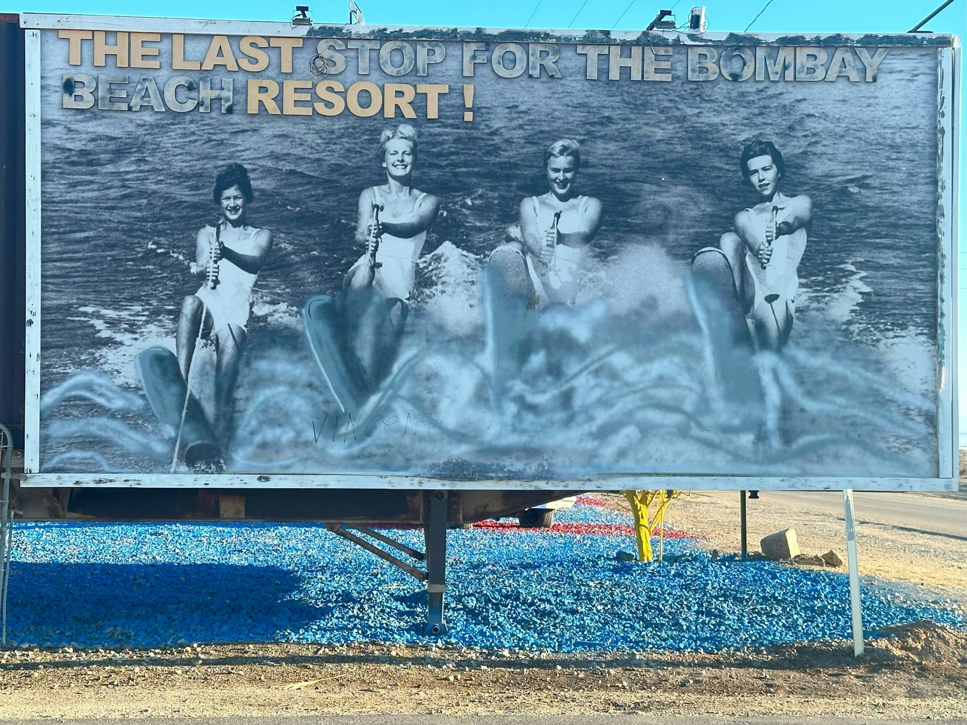 A faded and pealing billboard shows three women water skiing on a lake.