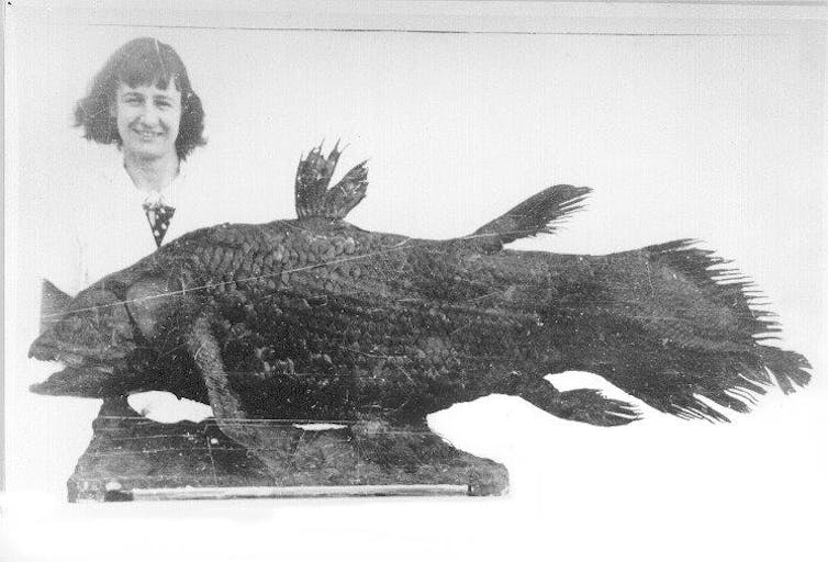 Old faded photo of a woman standing behind a large stuffed fish.