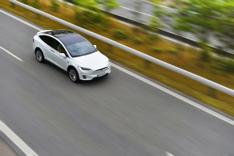 A Tesla electric vehicle drives at speed along a road