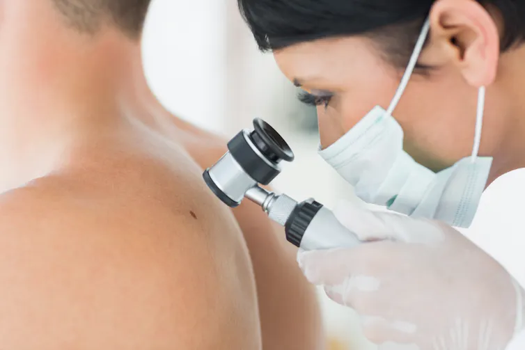 Un dermatologue examine un grain de beauté sur le dos d’un homme à l’aide d’une loupe