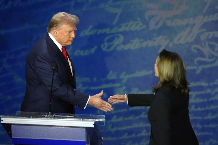 A white man and a Black woman shake hands.