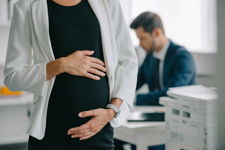 Pregnant woman standing in her workplace and holding her baby bump
