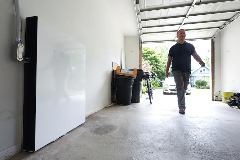A man walks into his garage, with a Tesla Powerwall battery on the left