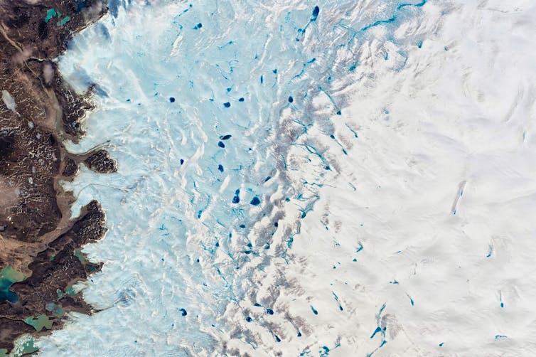 aerial shot of brown cliff, blue sea with white ice and oceberg on right side