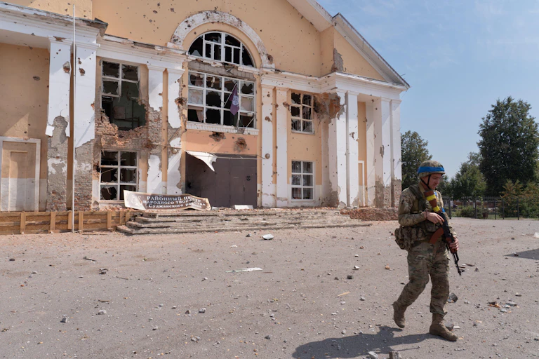 A Ukrainian soldier walks in front of a damaged building.