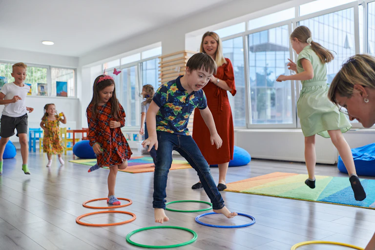 Children including boy with Down Syndrome jumping in hoops in classroom