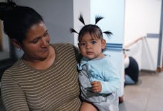 A young woman holds a baby girl with four pigtails sticking up around her head
