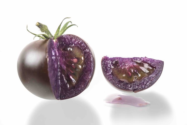 A purple tomato is sliced open to reveal purple flesh inside.