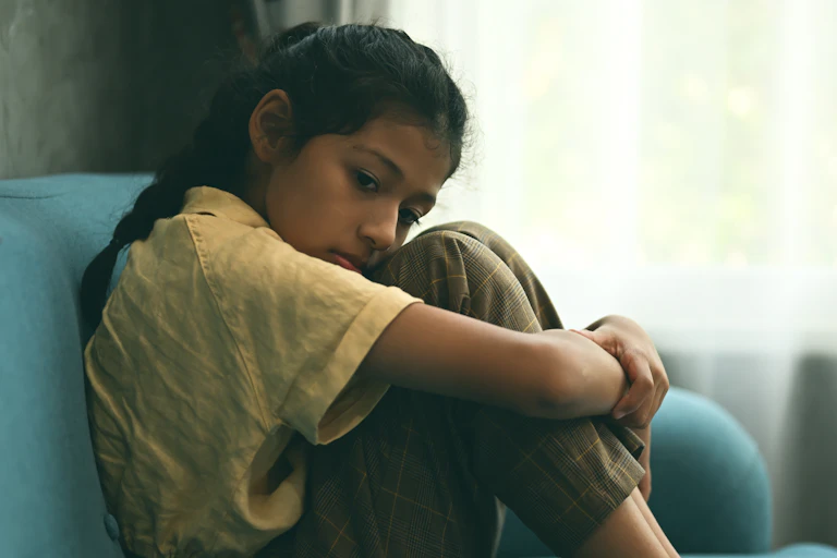 Sad girl hugs knees sitting on sofa