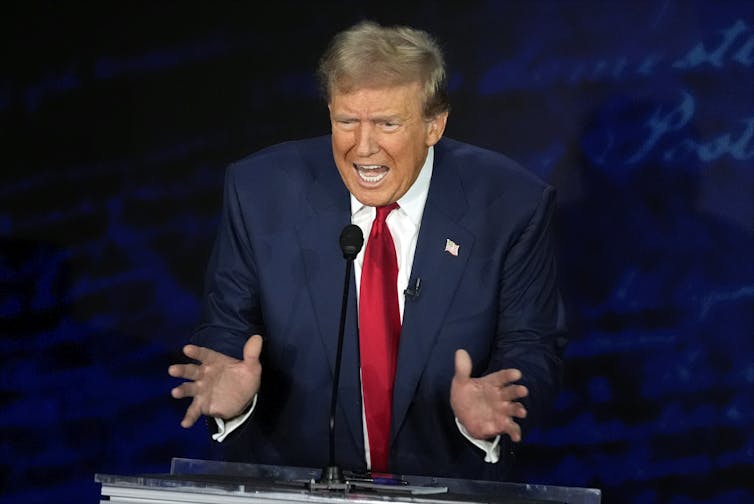 A grimacing man with gestures with his hands like he's playing an accordion.