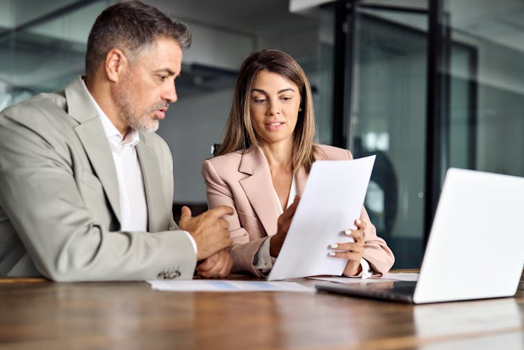 A man and woman sit at a desk looking over a sheet of paper