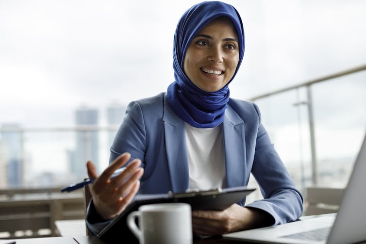 A woman in a blue suit and headscarf gestures with her hand while talking.
