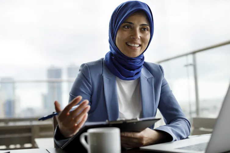 A woman in a blue suit and headscarf gestures with her hand while talking.