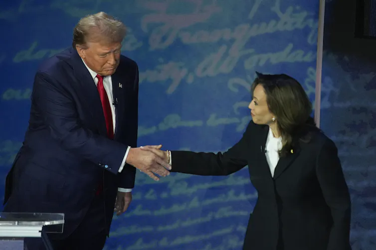 A dark-haired woman shakes hands with a rotund man with greyish-blond hair.